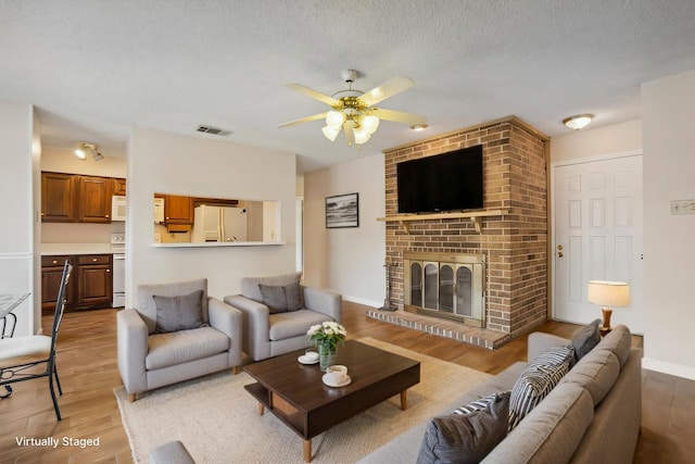 living area featuring a textured ceiling, a ceiling fan, visible vents, light wood-style floors, and a brick fireplace