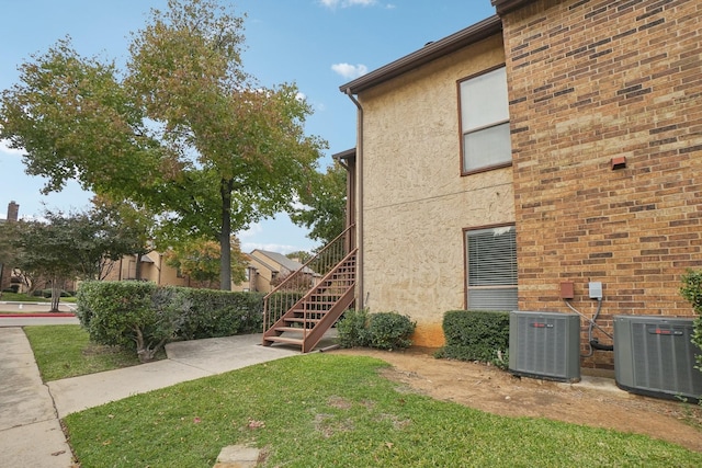 view of side of home featuring a yard, stairs, central AC unit, and stucco siding