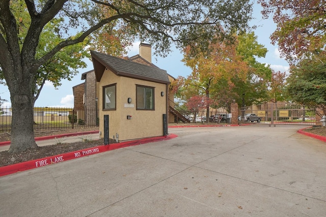 view of home's exterior featuring a shingled roof, fence, a chimney, and stucco siding