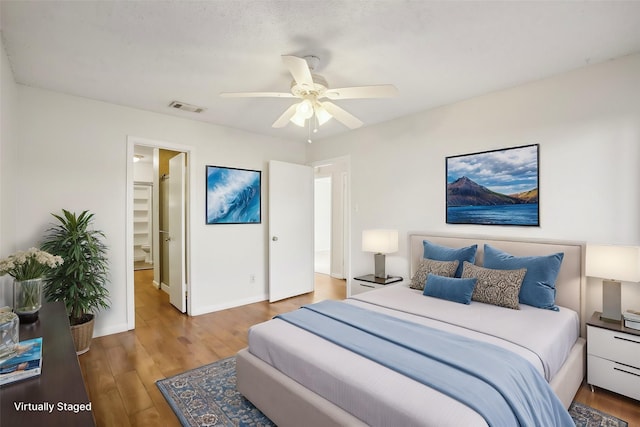 bedroom with wood finished floors, a ceiling fan, visible vents, baseboards, and ensuite bath