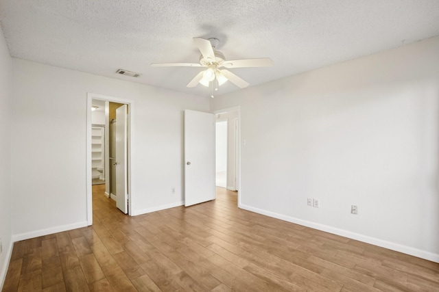 unfurnished bedroom featuring visible vents, baseboards, light wood-style flooring, a walk in closet, and a textured ceiling