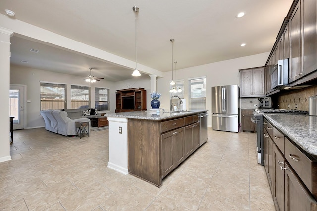 kitchen featuring light stone counters, stainless steel appliances, a sink, open floor plan, and decorative backsplash