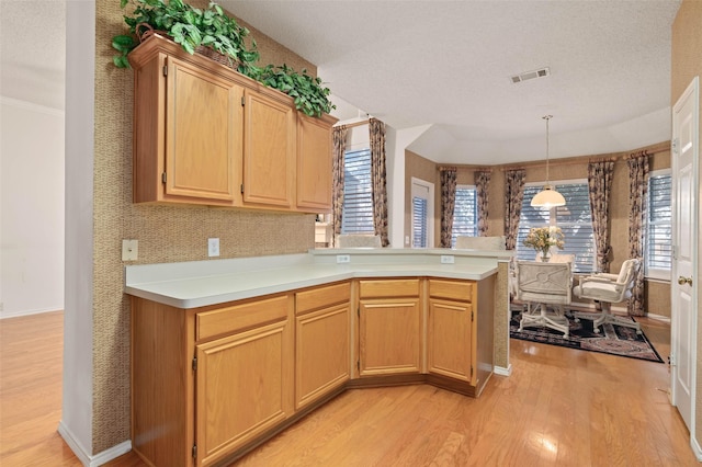 kitchen featuring light wood finished floors, visible vents, light countertops, a peninsula, and hanging light fixtures