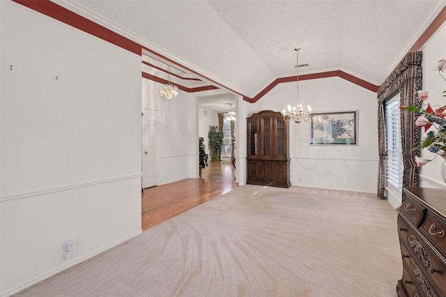 spare room with a notable chandelier, lofted ceiling, light colored carpet, and crown molding