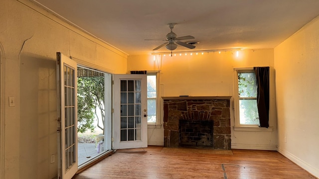 unfurnished living room featuring ceiling fan, a fireplace, baseboards, and wood finished floors