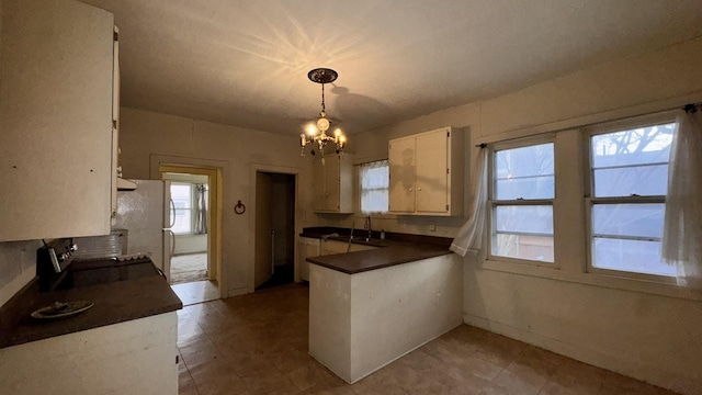 kitchen with a notable chandelier, dark countertops, white cabinetry, a sink, and a peninsula