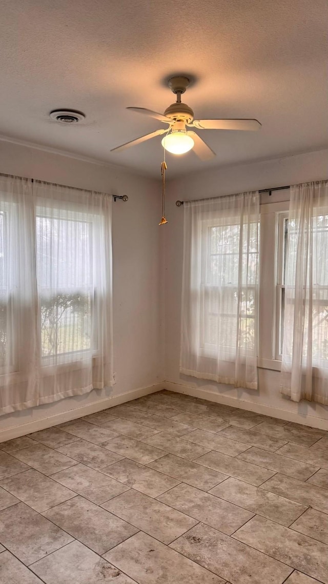 empty room featuring a textured ceiling, a wealth of natural light, visible vents, and a ceiling fan