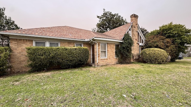 view of front of home featuring brick siding, a chimney, a front yard, and a shingled roof