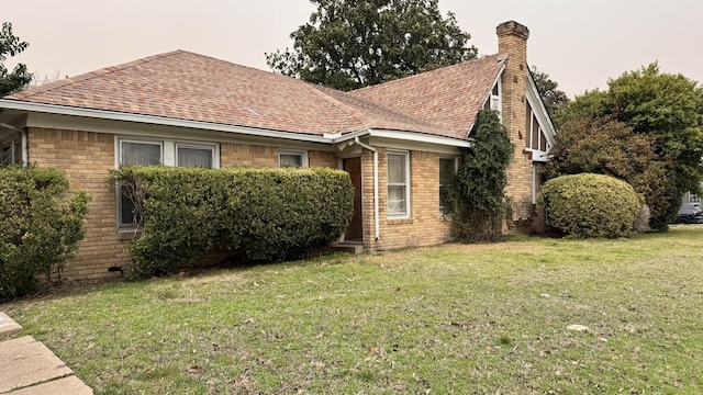 view of front of home with a shingled roof, a front yard, brick siding, and a chimney