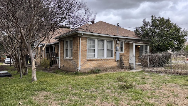 bungalow-style house with entry steps, brick siding, roof with shingles, and a front yard