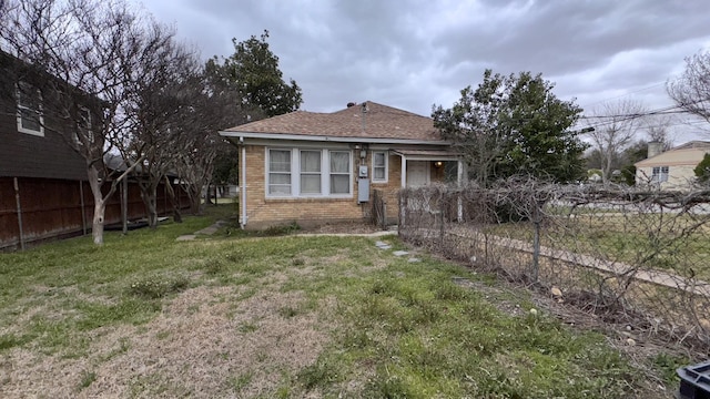 back of property featuring roof with shingles, fence, a lawn, and brick siding