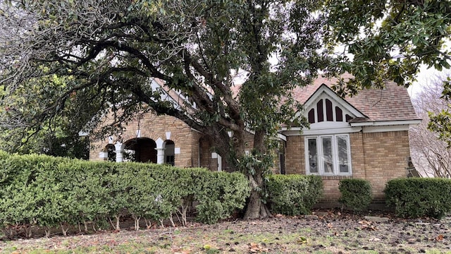 tudor house featuring brick siding and roof with shingles