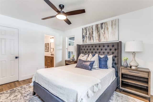 bedroom featuring baseboards, a ceiling fan, wood finished floors, ensuite bathroom, and a sink