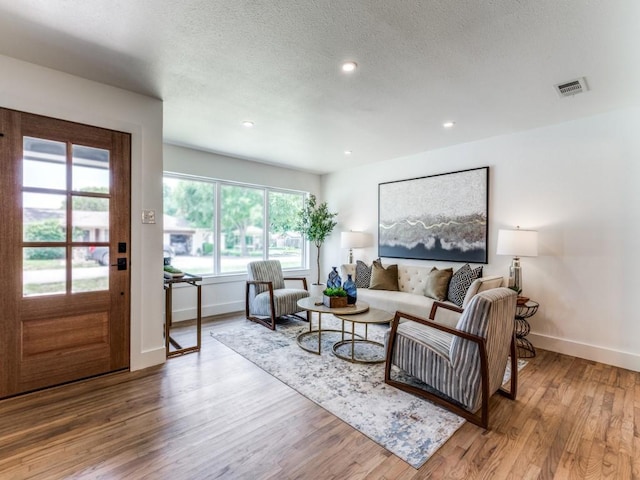 living area with a textured ceiling, recessed lighting, wood finished floors, visible vents, and baseboards