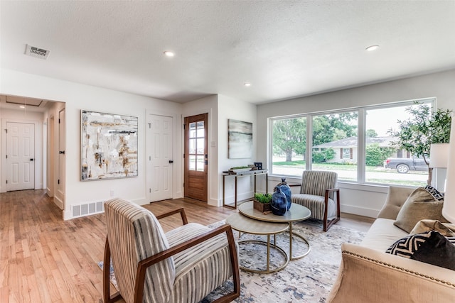 living room with visible vents, a textured ceiling, light wood-type flooring, and attic access