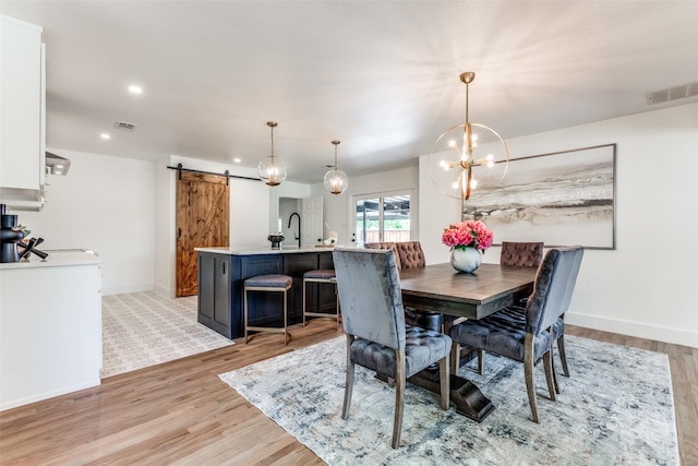 dining room with light wood-style floors, a barn door, visible vents, and baseboards