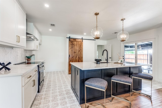 kitchen with a barn door, under cabinet range hood, electric range, white cabinetry, and visible vents