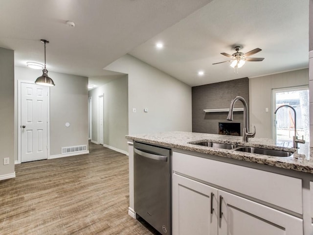 kitchen with dishwasher, light stone counters, light wood-style floors, white cabinetry, and a sink