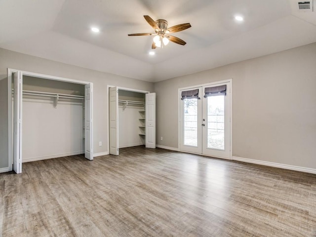 unfurnished bedroom with french doors, multiple closets, lofted ceiling, visible vents, and wood finished floors