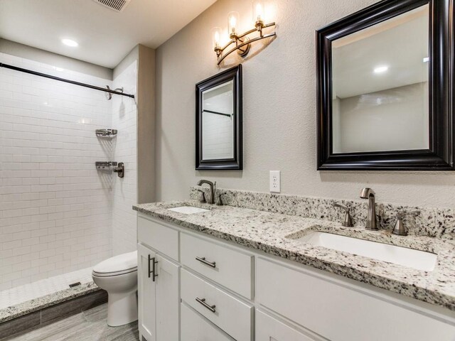 bathroom featuring tiled shower, a sink, toilet, and double vanity