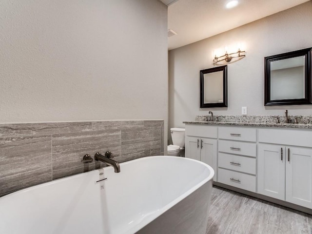 bathroom with double vanity, a soaking tub, toilet, a sink, and wood finished floors