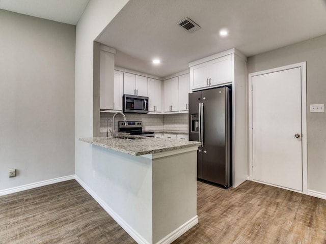 kitchen featuring a peninsula, a sink, white cabinets, appliances with stainless steel finishes, and light stone countertops