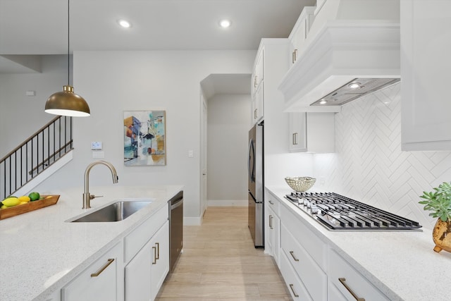 kitchen with white cabinets, appliances with stainless steel finishes, light stone countertops, custom exhaust hood, and a sink