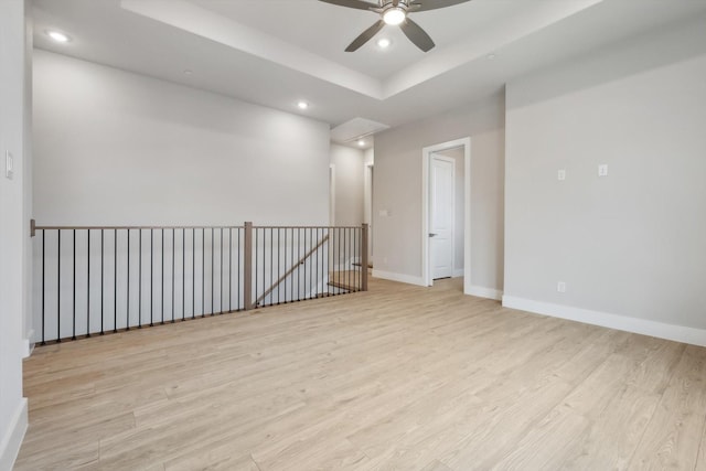 empty room featuring a tray ceiling, recessed lighting, wood finished floors, and baseboards