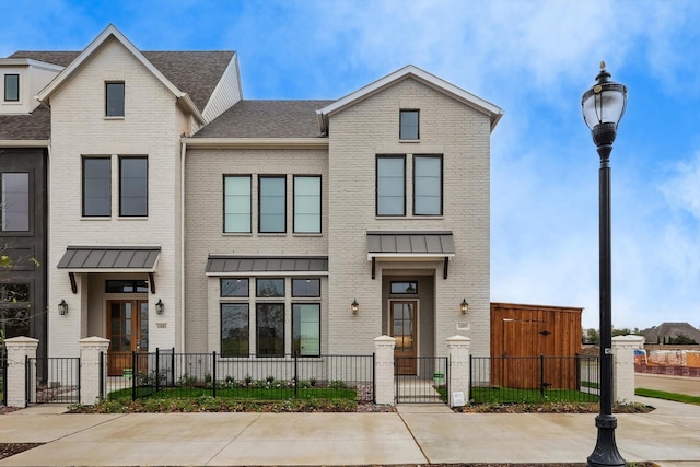 townhome / multi-family property featuring a standing seam roof, a fenced front yard, a gate, and brick siding