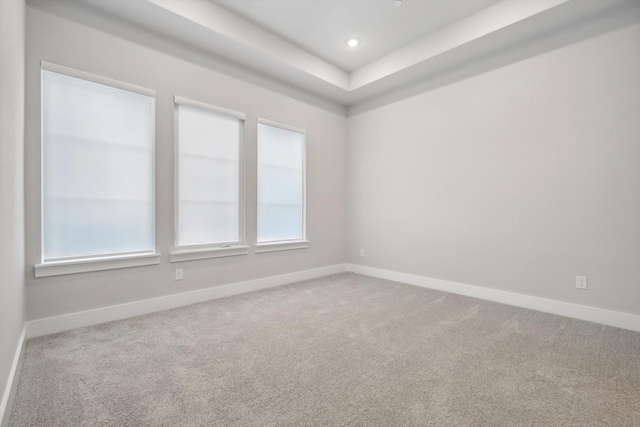 empty room featuring a tray ceiling, recessed lighting, carpet, and baseboards