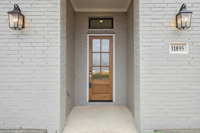 entrance to property with roof with shingles and brick siding