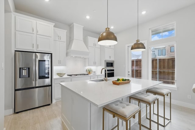 kitchen with tasteful backsplash, custom range hood, a kitchen island with sink, stainless steel appliances, and a sink