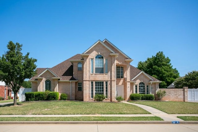 traditional home featuring brick siding, a front yard, and fence