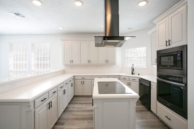 kitchen featuring light wood-type flooring, black appliances, visible vents, and island range hood