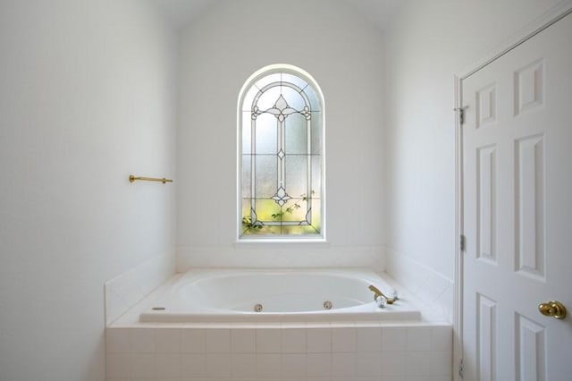 bathroom featuring lofted ceiling, a tub with jets, and a wealth of natural light