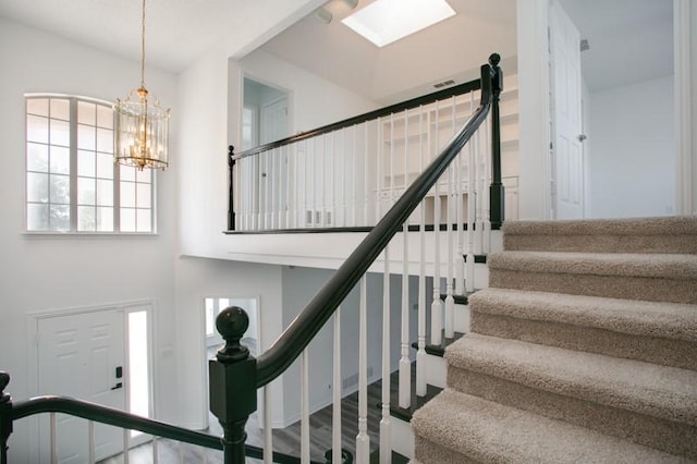 staircase featuring a towering ceiling, a skylight, visible vents, and a chandelier