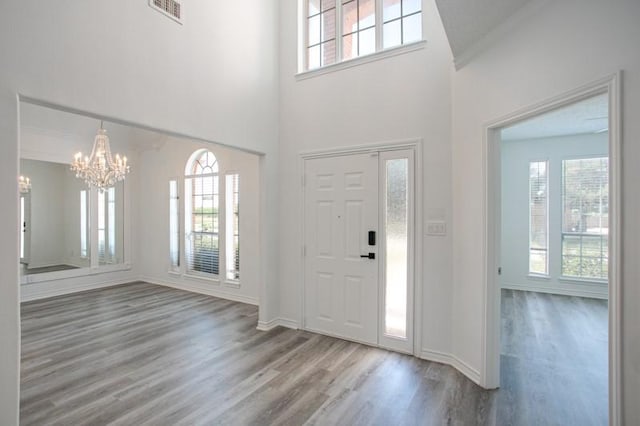 foyer entrance with a wealth of natural light, visible vents, a chandelier, and wood finished floors