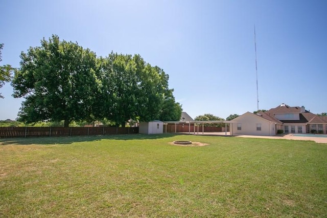 view of yard featuring a storage shed, a fenced backyard, an outdoor fire pit, and an outbuilding