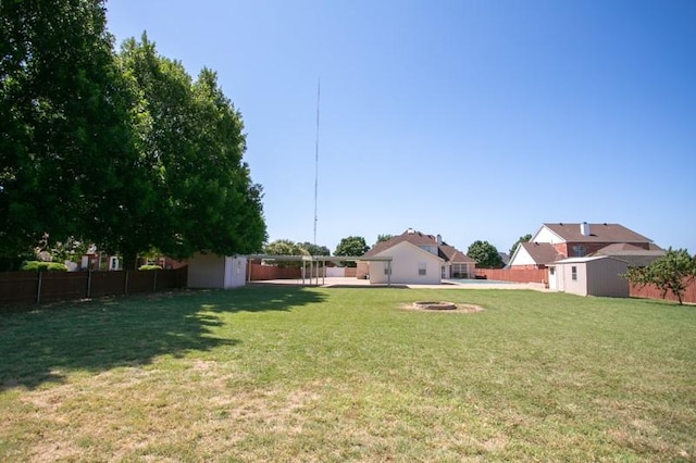 view of yard featuring a fire pit, a fenced backyard, a storage unit, and an outbuilding