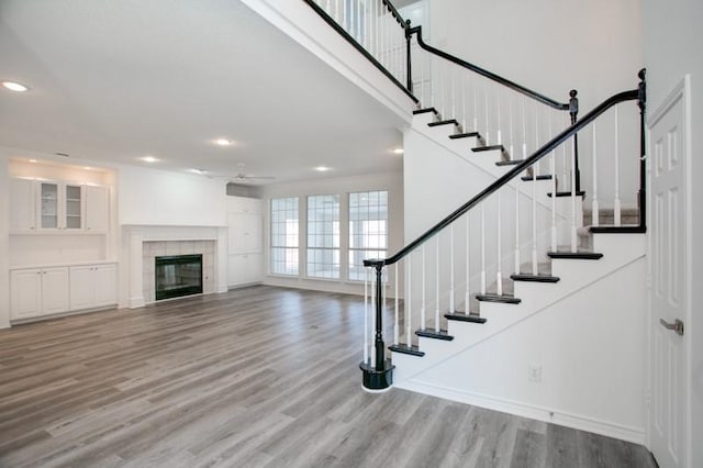 staircase featuring recessed lighting, a towering ceiling, a ceiling fan, wood finished floors, and a tile fireplace