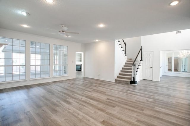 unfurnished living room with visible vents, stairway, wood finished floors, and ceiling fan with notable chandelier