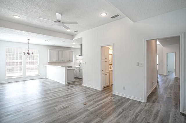 unfurnished living room with baseboards, visible vents, wood finished floors, and ceiling fan with notable chandelier