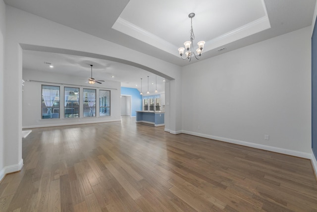 unfurnished living room featuring arched walkways, wood finished floors, a raised ceiling, and baseboards