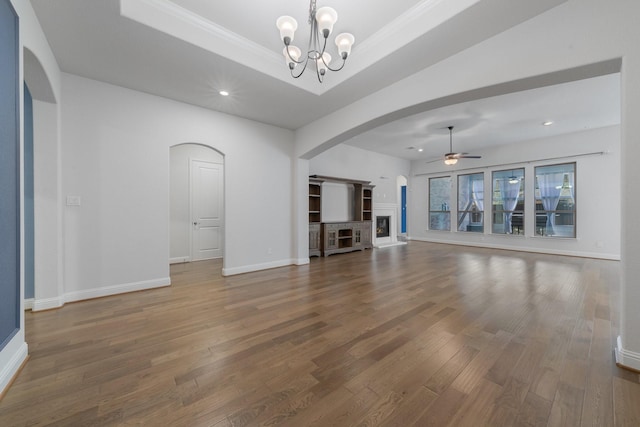 unfurnished living room with arched walkways, a tray ceiling, ceiling fan with notable chandelier, and wood finished floors