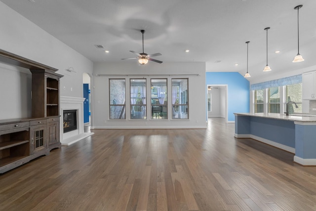 unfurnished living room featuring dark wood-style floors, baseboards, a glass covered fireplace, and lofted ceiling