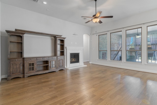 unfurnished living room with baseboards, a ceiling fan, wood finished floors, and a glass covered fireplace