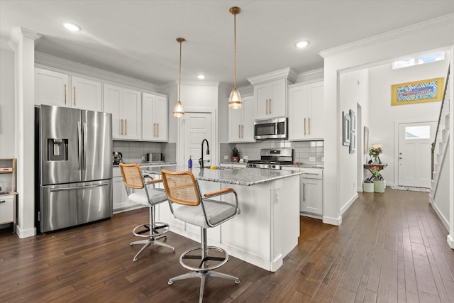 kitchen with stainless steel appliances, white cabinets, ornamental molding, light stone countertops, and dark wood-style floors