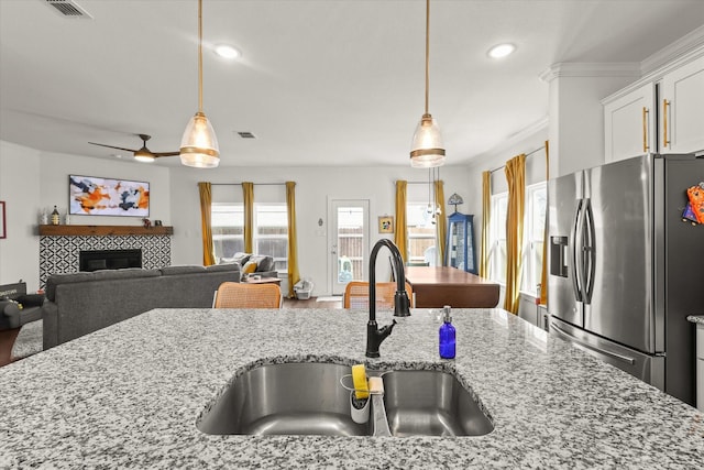 kitchen with pendant lighting, a sink, light stone countertops, a tile fireplace, and stainless steel fridge with ice dispenser