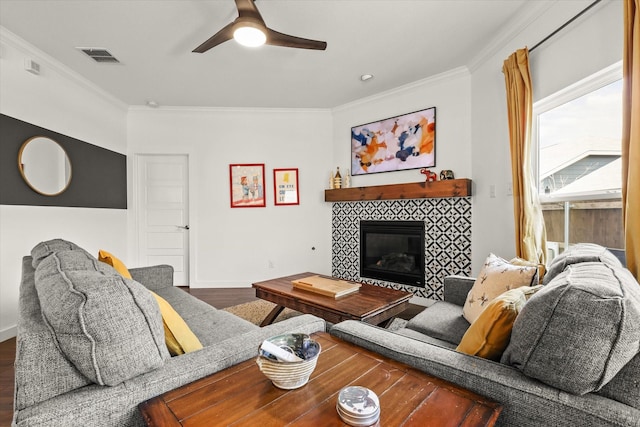 living area with ceiling fan, a tiled fireplace, ornamental molding, and wood finished floors