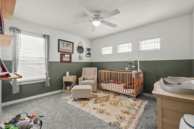 bedroom with a nursery area, baseboards, ceiling fan, and carpet